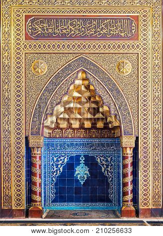 Cairo, Egypt - October 21, 2017: Golden ornate arched mihrab (niche) with floral pattern blue Turkish ceramic tiles and arabic calligraphy at the public mosque of The Manial Palace of Prince Mohammed Ali Tewfik Cairo Egypt