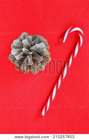 Snow dusted pine cone and candy cane on textured red background shot from overhead in vertical format
