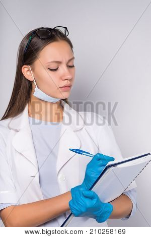 a young girl in a medical white coat and a face mask, glasses focussively fills out medical documents