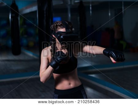 Young fighter boxer fit girl in VR glasses wearing boxing gloves in training. Boxing game in virtual reality 360 degrees. Futuristic gaming vr concept
