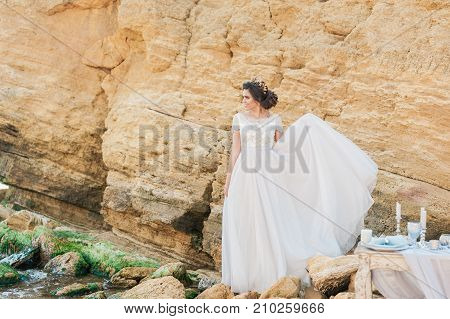 Beautiful brunette bride in light chiffon wedding dress embroidered with beads posing near the sea. Romantic beautiful bride in luxury dress posing on the beach.