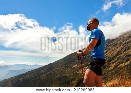 Sporty guy traveler in a blue t-shirt on a background of a beautiful sky with clouds in the mountains.