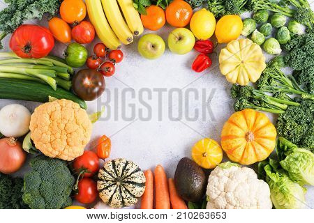 Assorted colorful vegetables and fruits arranged in a circle on the light grey background, copy space for text in the middle, selective focus
