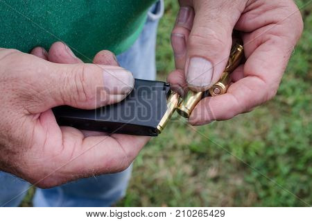 Working mans hands loading bullets into clip in preparation of sport target shooting. Handgun ammunition also used for self defense against crime and violence.