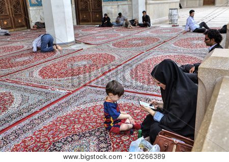 Shiraz Iran - 19 april 2017: Iranian Muslim woman dressed in a chador with her child a boy of five years old rests in the inner courtyard of the mosque near Islamic men rest and pray.