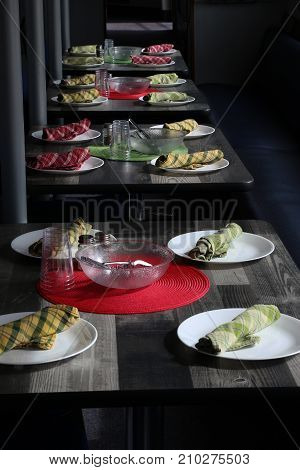 Four black tables in a boat's galley each set with four place settings consisting of colorful plaid napkins, place mats,and white plates for lunch. Vertical photo.
