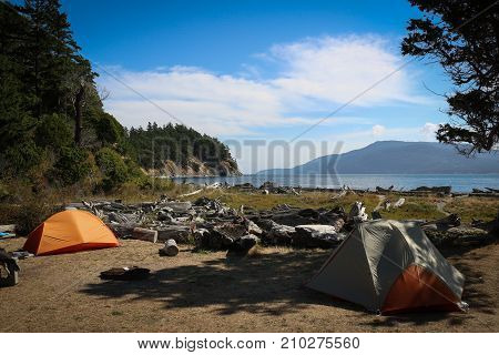 Two tents set in a campsite on Sucia Island, San Juan Islands, Washington State, looking across the water to Orcas Island against a blue sky with white clouds.