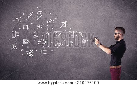 An elegant hipster guy trying to use a vintage camera with camera settings icons drawn on wall, like flash, white balace or ISO value concept