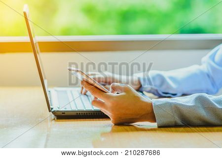 Businessman working with smart phone and laptop computer on wooden desk ; remote working concept; home business concept.