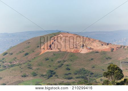 Industrial earthworks sand quarry machine excavators and trucks cutting extracting soil away countryside hillside for engineering contruction building projects.