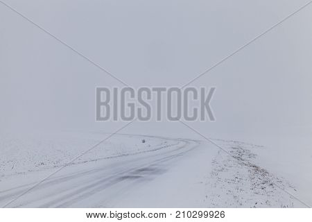 Narrow Road Covered With Snow. On The Surface Of The Asphalt A Few Tracks, Fog And Snow In The Dista
