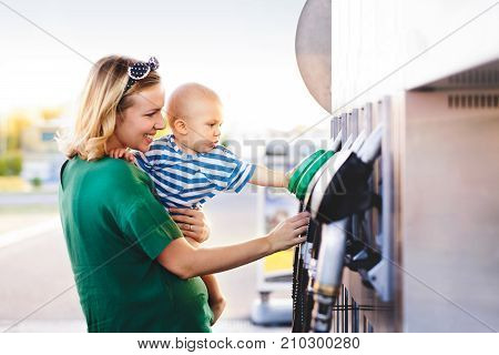Young mother with baby boy at the petrol station going to refuel the car.