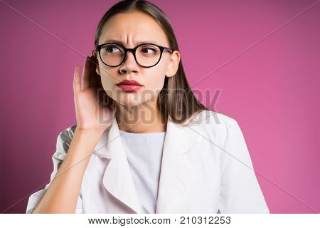 a girl in a white robe and in big glasses listens to extraneous sounds and looks to the side, in isolation