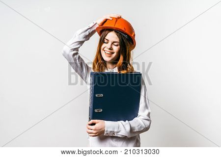 cute girl in orange helmet and with big folder in hands. Gerl holds his helmet with his hand and laughs