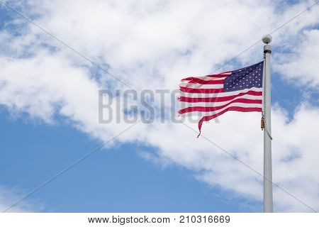 Weathered American flag on a pole with blue sky background. Old flag flapping in the wind on pole. Fourth of July Patriotism. Worn out American flag. July 4th