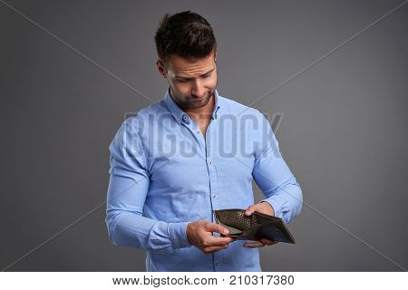 A poor handsome young man feeling stressed while looking at his empty wallet.