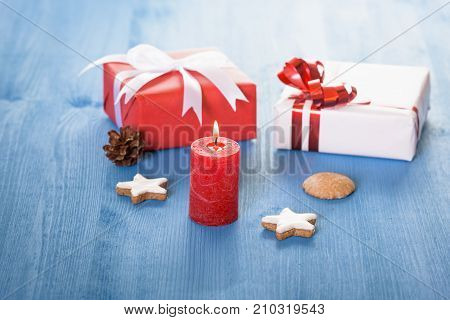 Gifts and red candle on blue table - Christmas decor with small gift boxes gingerbread cookies and a lit red candle