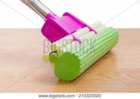 Green sponge on plastic mop with mounting clamp closeup on a wooden floor on a white background