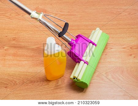 Liquid floor cleaner in plastic bottle and plastic mop with mounting clamp and green sponge on a wooden floor