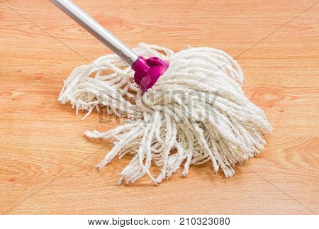 Cotton head of the classic mop with metal tubular handle n a wooden floor