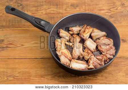 Fried pork ribs on the cast aluminium frying pan with ceramic non-stick coating on a surface of old planks