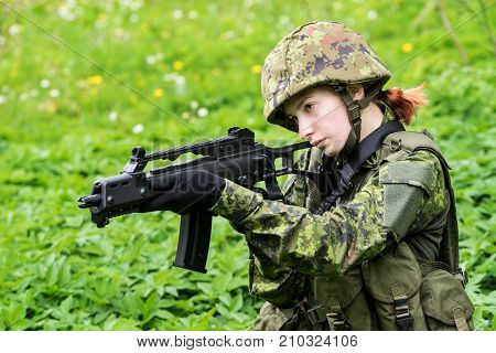 Portrait of armed woman with camouflage. Young female soldier observe with firearm. Child soldier with gun in war green goutweed background. Military army people concept