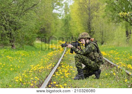 Portrait of armed woman with camouflage. Young female soldier observe with firearm on rail. Child soldier with gun in war green grass and yellow dandelions background. Military army people concept