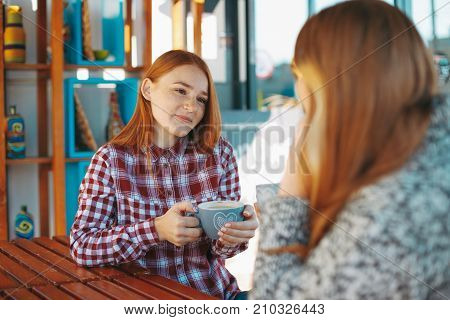 People, communication and friendship concept -girls chating while drinking coffee at outdoor cafe. Two natural reddish girls having coffee.