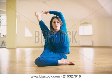Beautiful woman practices yoga sitting twisted asana Marichiasana in the yoga studio.