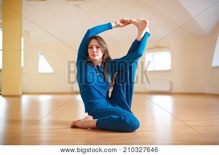 Beautiful woman practices yoga sitting twisted asana Marichiasana in the yoga studio.