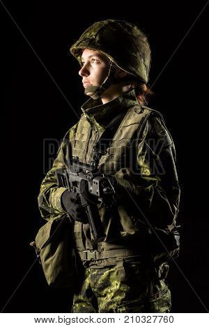 Portrait of armed woman with camouflage. Young female soldier observe with firearm. Child soldier with gun in war black background. Military army people concept