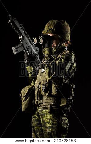 Portrait of armed woman with camouflage. Young female soldier observe with binoculars. Child soldier with gun in war black background. Military army people concept