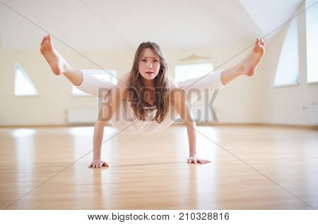 Beautiful woman practices handstand yoga asana Tittibhasana - firefly pose in the yoga studio.