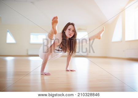 Beautiful woman practices handstand yoga asana Tittibhasana - firefly pose in the yoga studio.