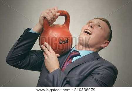 Debt. Debentures. Business man holding in his hands kettlebell with DEBT inscription isolated on grey background.