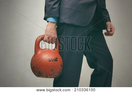Debt. Debentures. Business man holding in his hands kettlebell with DEBT inscription isolated on grey background.