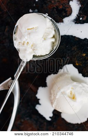 Melted ice cream in metal ice cream scooper over black rustic table