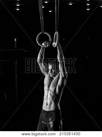 Muscular young shirtless man doing intense workout on gymnastics rings. Strength or callistenics workout. Fitness, sports concept.
