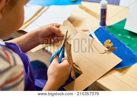 High angle portrait of unrecognizable little boy cutting paper in arts and crafts class of pre-school making handmade gift