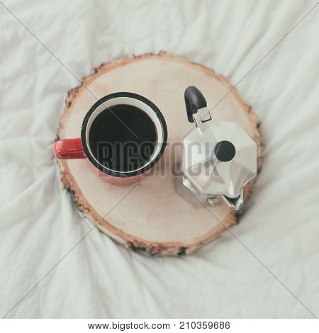 Coffee mug with steel coffee maker on wooden tray on white bed sheet. Top view. Flat lay