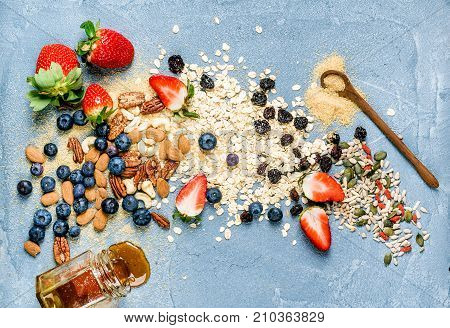 Ingredients for cooking healthy breakfast. Strawberries, blueberries, nuts, oat flakes, dried fruits, honey with drizzlier over concrete textured background, top view