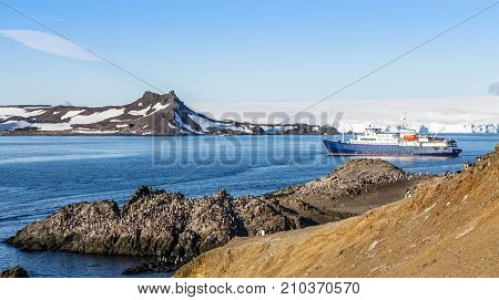Blue antarctic cruise ship in the lagoon and Gentoo penguins colony on the rocky shore of the Barrientos Island Antarctica