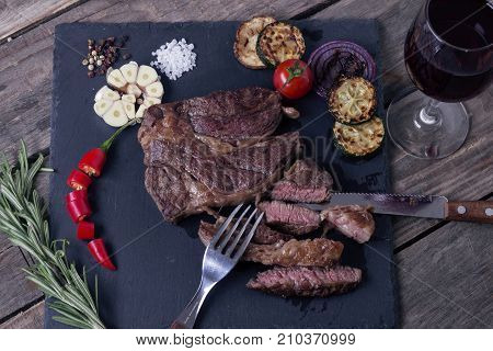 Grilled beef striploin steak from black angus and vegetables on stone plate. Salt and papper. Glass of vine. Top view