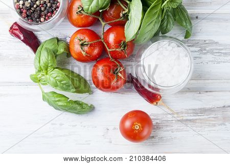Tomatoes bunch of fresh green basi pepper and saltl on a whute wood background Fresh aromatic herbs close up Culinary cooking herbs. Copy space