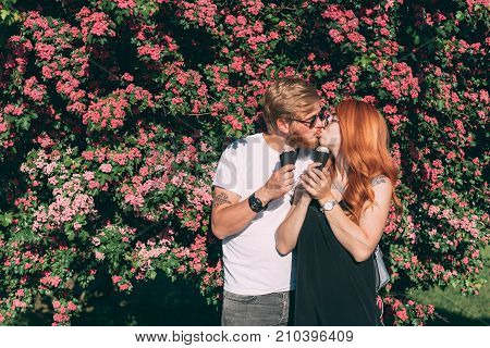Couple in park eating ice cream cones, posing on camera