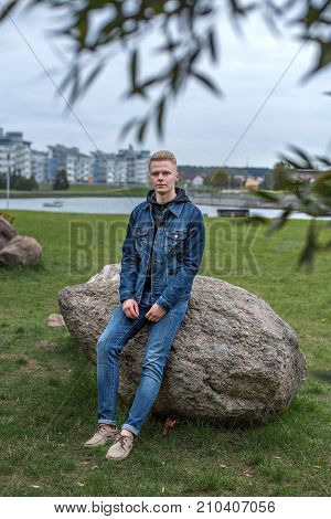 nice guy in jeans jacket sits on a stone in the park in a nightfall
