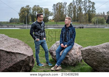 university pupils are sitting on stones and talking in the city park in nightfall