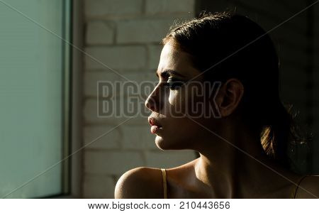 Girl or woman with face profile look at window on white brick wall. Contemplation loneliness solitude depression concept.