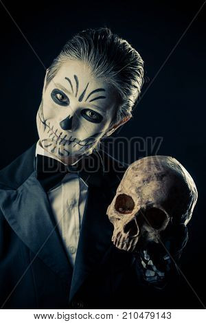 Portrait of a child boy with carnival make-up of a skeleton wearing elegant tail-coat. Studio shot over black background. Halloween. Dia de los muertos. The Day of the Dead.