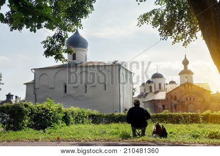 A man looking of the old church at sunlight. Assumption Church and the Church of Paraskeva Friday at the Trade Courtyard  in Veliky Novgorod, Russia.